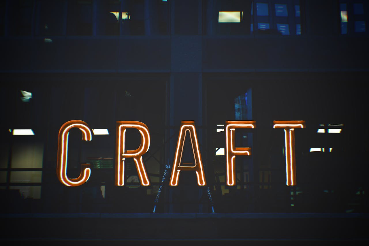Illuminated neon sign with the word 'CRAFT' glowing against a building backdrop.